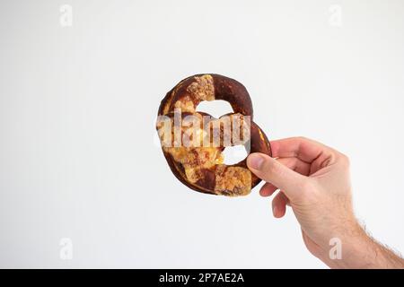 Freshly home backed Pretzel held in hand by Caucasian male hand. Close up studio shot, isolated on white. Stock Photo
