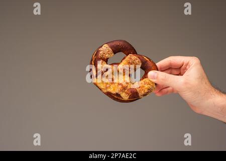 Freshly home backed Pretzel held in hand by Caucasian male hand. Close up studio shot, isolated on gray. Stock Photo
