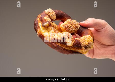 Freshly home backed Pretzel held in hand by Caucasian male hand. Close up studio shot, isolated on gray. Stock Photo