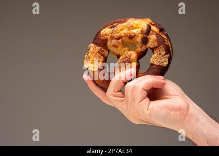Freshly home backed Pretzel held in hand by Caucasian male hand. Close up studio shot, isolated on gray. Stock Photo