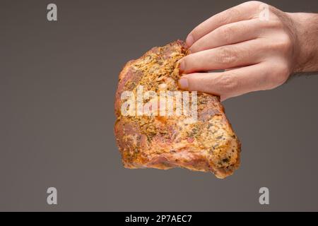 Raw rack of seasoned pork ribs held in male hand close up shot, isolated on brown background. Studio shot. Stock Photo