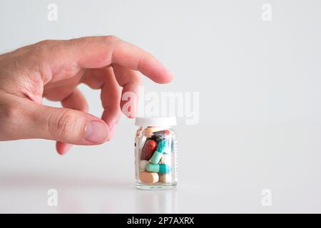 Caucasian male hand reaching out for a glass bottle full of various colored medical pills, tablets and capsules. Close up studio shot, isolated on whi Stock Photo