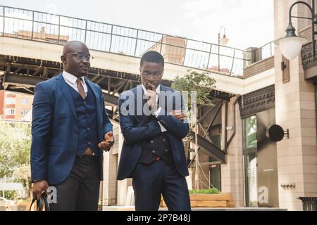Two dark-skinned african american businessmen in suits with briefcases walk along the city street Stock Photo