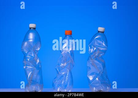 3 large clear squeezed plastic water bottles with close caps. Studio shot, isolated on blue, no people. Stock Photo