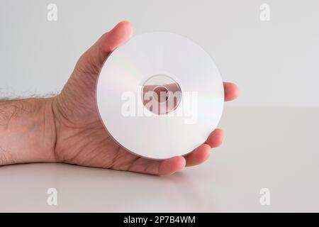 Compact Disc DVD held in hand by Caucasian male hand. Writable side view, close up studio shot, isolated on white. Stock Photo