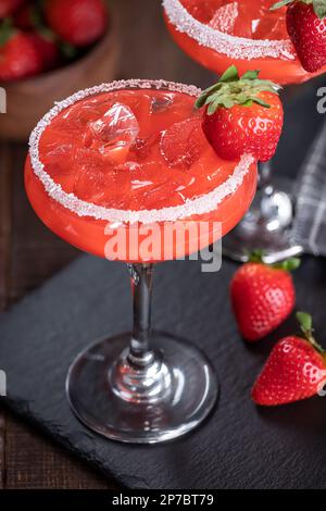Strawberry margarita cocktail garnished with strawberries and salt rim on a black slate board Stock Photo