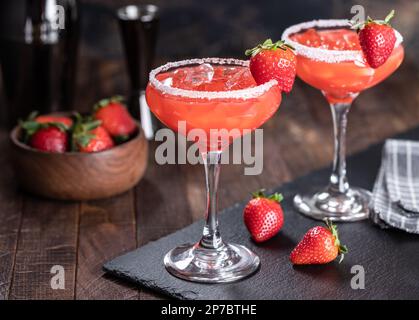 Strawberry margarita cocktail garnished with strawberries and salt rim on a black slate board Stock Photo