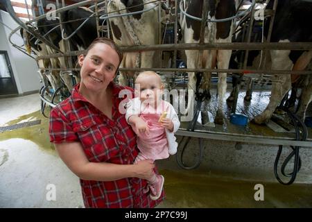 Farmer's wife and daughter standing next to dairy cows during milking Rotary milking parlour / shed 50 standings Holstein Friesian dairy cows New Zeal Stock Photo