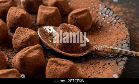 Chocolate truffle ball on a spoon closeup. Plate of dark chocolate candy sprinkled with cocoa powder. Homemade confection recipe, gourmet dessert. Stock Photo