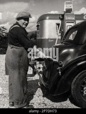 Vintage photograph taken in 1950 at the Lochy Bridge Petrol Station at Fort William, western Highlands, Scotland, UK.  Pump attendant wearing a flat cap and expansive trousers held up by braces or suspenders refuels a black car with Regent petrol, a brand that disappeared from British forecourts in 1969 after being taken over by Texaco in 1956. Stock Photo