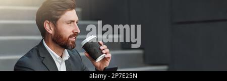 Attractive office worker in suit sitting on stairs with coffee during break and using phone Stock Photo