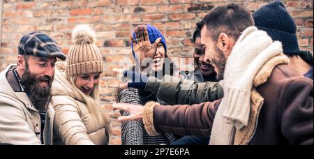 International friends giving five together wearing warm fashion clothes - Happy lifestyle concept with multicultural millennial people having fun toge Stock Photo