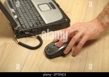 a person holds a computer mouse on hand next to an old laptop Stock Photo