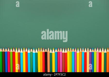 multicolored pencils is on green chalkboard background, top view, copy space, back to school concept. Stock Photo