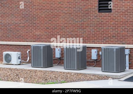 Horizontal shot of four air conditioning compressors outside a school building. Stock Photo