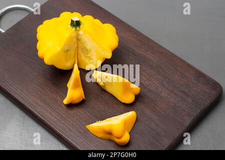 Yellow round zucchini and zucchini slices on a cutting board. Top view. Gray background. Stock Photo