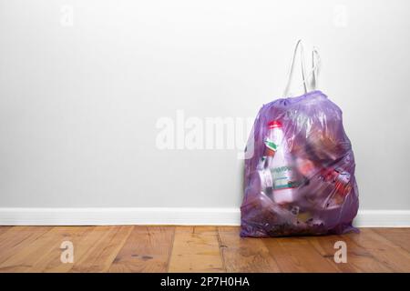 Purple garbage bag at home on a wooden floor near a gray wall. House cleaning. Garbage sorting theme. Caring for the environment. Stock Photo