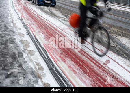 Motion blurred cyclist cycling on slippery bike path / cycle path covered in sleet during unexpected late snow shower in March 2023, Ghent, Belgium. M Stock Photo