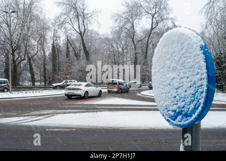 Cars on busy slippery intersection and road sign covered in snow during unexpected late sleet and snow shower in March 2023, Gent, Belgium Stock Photo