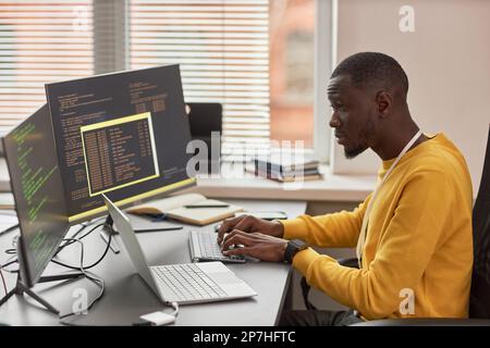 Side view portrait of young black man typing at keyboard and writing code in IT development company Stock Photo