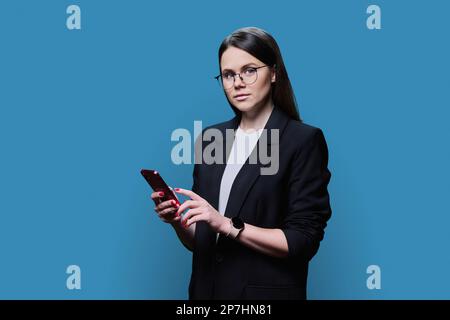 Young business woman using smartphone on blue studio background Stock Photo