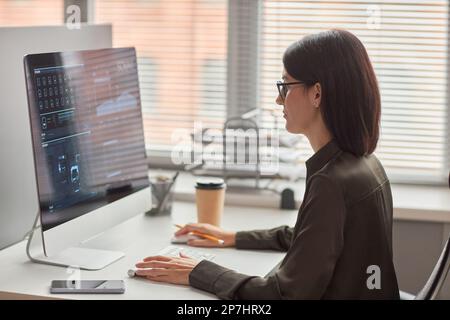 Side view portrait of young woman working with data analysis at minimal workplace in office against window, copy space Stock Photo