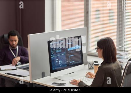 High angle view of two office workers at desk with partition wall, focus on data on computer screen Stock Photo