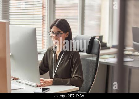 Portrait of businesswoman wearing glasses while using computer at workplace in office, copy space Stock Photo