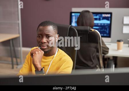 Portrait of focused black man looking at computer screen in office, copy space Stock Photo