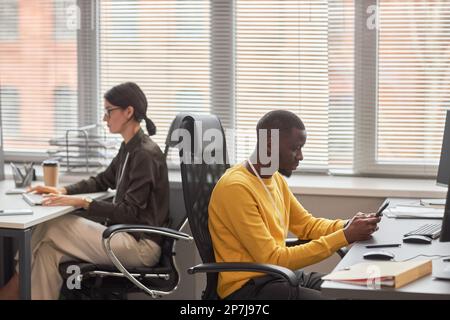 Side view portrait of two office workers at desks back to back working in office Stock Photo