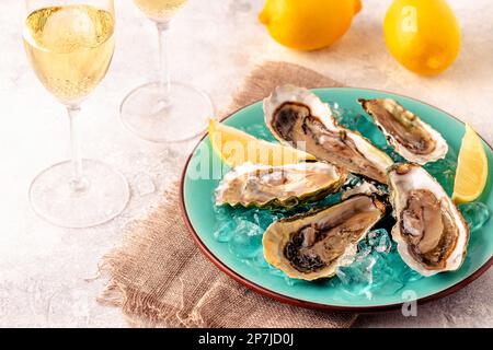 Opened fresh oysters on a blue plate, served with lemon and ice. Stock Photo