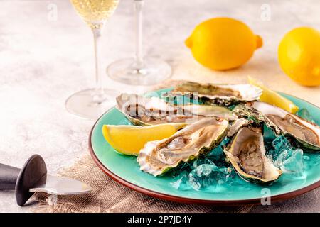 Opened fresh oysters on a blue plate, served with lemon and ice. Stock Photo