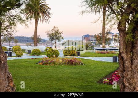 Tropical trees, bushes and lawns in a public park Jardines de Piquio at sunset, with the city view in the background. Santander, Cantabria, Spain. Stock Photo