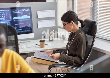 Side view portrait of female data scientist working with documentation at desk in office Stock Photo