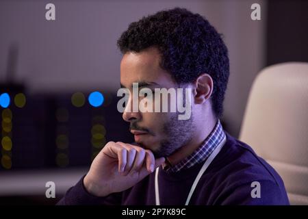 Side view portrait of focused man thinking while working on IT project in office lit by neon light Stock Photo