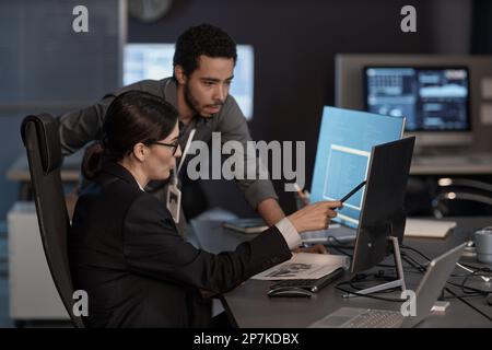 Side view portrait of two people pointing at computer screen while working in IT company Stock Photo