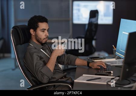 Side view portrait of man using computer and drinking coffee while working in data security office Stock Photo