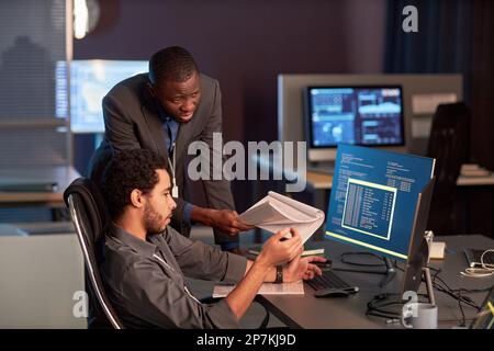 Two male IT engineers discussing documentation at workplace in office and reviewing code Stock Photo