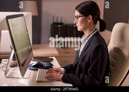 Side view portrait of serious businesswoman using computer while working at night in IT security office Stock Photo