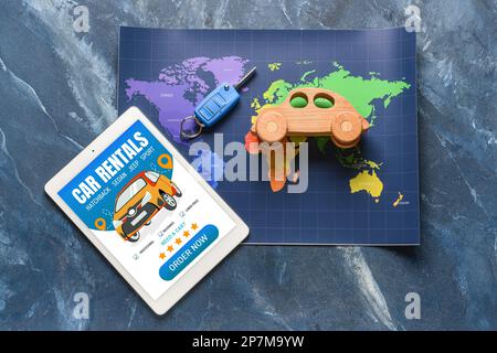 Tablet computer with open page of car rental website, map, key and toy car on blue background Stock Photo