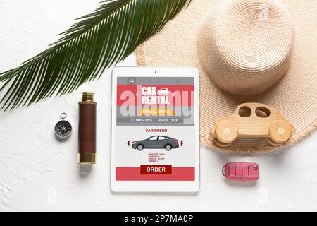 Composition with open page of car rental website on tablet computer, beach hat and key on white background Stock Photo