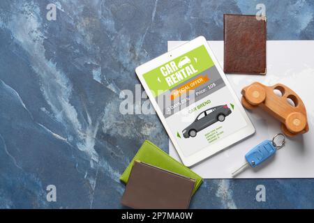 Tablet computer with open page of car rental website, map, key and passports on blue background Stock Photo