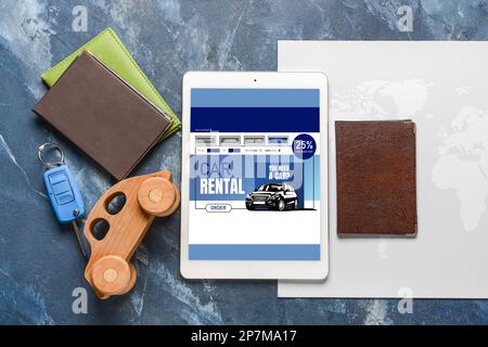 Tablet computer with open page of car rental website, map, key and passports on blue background Stock Photo