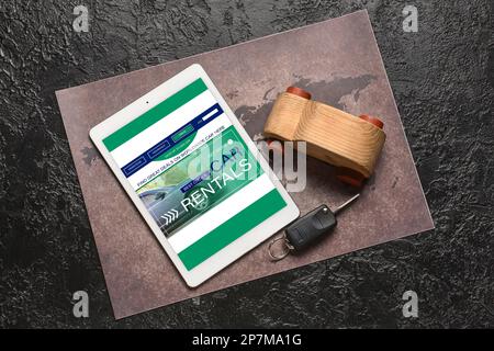 Tablet computer with open page of car rental website, map, toy car and key on dark background Stock Photo
