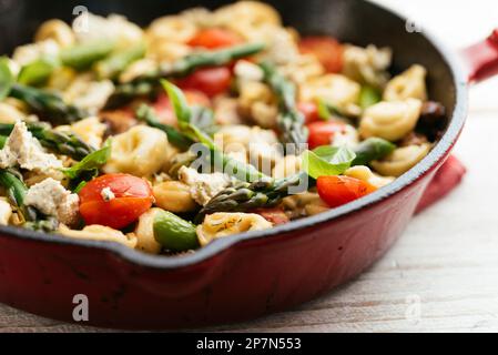 Cast iron pan with vegetable tortellini with asparagus, tomatoes, mushrooms and home made vegan feta cheese. Stock Photo