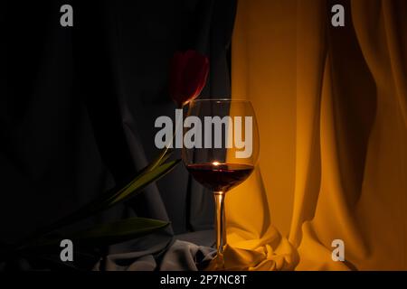 Tulip and a glass with red wine on the background of the flag of Ukraine in the dark, culture Stock Photo