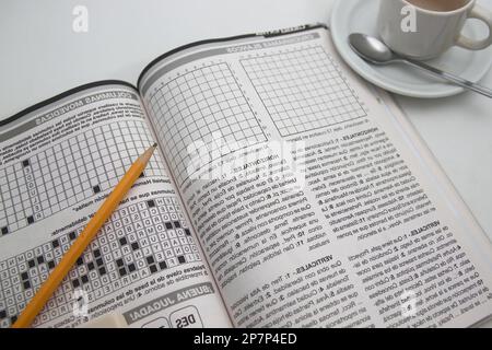 Image from above of a black and white printed page with crosswords and brain teasers next to a cup of coffee and a pencil Stock Photo