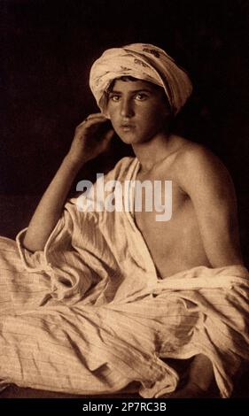 1905 ca , Tunis , Tunisia : Orientalis photo of tunisian boy by  celebrated french-austrian duo pictorialist photographers  Rudolf LEHNERT ( 1878 - 1948 ) and Ernst LANDROCK  ( 1878 - 1966 ) . Image pubblished like postcard photogravure - MAGREB - NORTH AFRICA - NORD AFRICA - ORIENTALISMO - ORIENTALISTA - ORIENTALISM - ORIENTALIST - Harem  - ARTI VISIVE - FOTOGRAFO - FOTOGRAFIA - ARTE - PHOTOGRAPHY   - ART - AUTORITRATTO - portrait - ritratto  - boy - ragazzo - uomo - VASE - VASO - VASAIO - ETHIC - ETNICO - ETNOGRAFIA - ETHNOGRAPHY - ETNOLOGIA - ETHNOLOGY - ARABIAN - ARABO - COLONIALISMO - COL Stock Photo