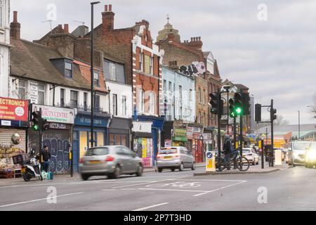 Pedestrians and vehicles cross a street in Peckham, London, SE15.  Traffic lights show a green pedestrian signal. Stock Photo