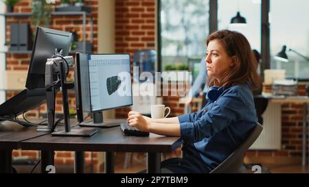 Female engineer working on turbine component development, using professional manufacturing software. Agency employee developing 3d engine component with infographics, creative skills. Stock Photo